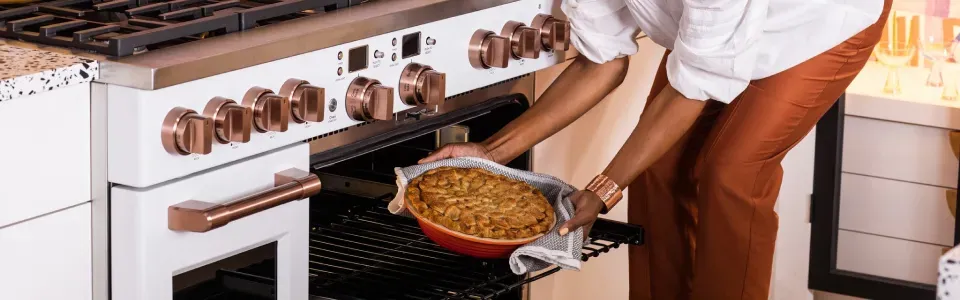 woman pulling out a baked apple pie out of the oven